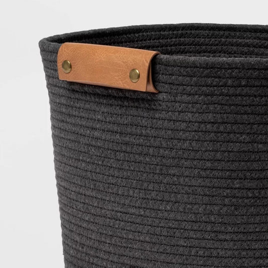 Close-up of the Brightroom™ gray rope basket's side, showing the intricate coiled design and one leather handle with brass fixtures.