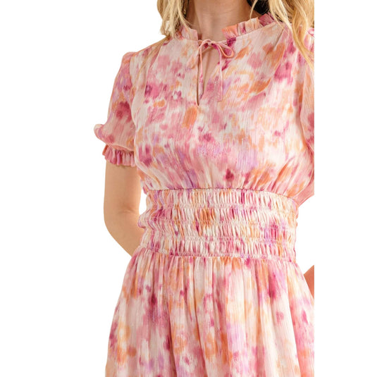 Close-up of the upper part of a pastel pink and orange floral dress. The dress features a high neckline with a tie, short puff sleeves with ruffled edges, and a smocked waist that provides a flattering fit. The intricate floral pattern adds a touch of whimsy and femininity.