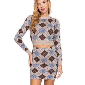 Woman standing posed in a coordinated outfit consisting of a taupe and blue argyle patterned mini skirt and crop top sweater set.