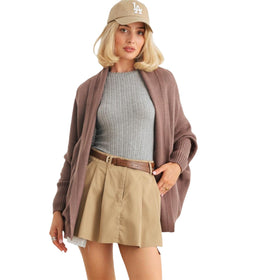 A model in a cozy knit cardigan with batwing sleeves and ribbed texture, styled over a grey top and khaki skirt, accessorized with a beige baseball cap, showcasing a casual yet stylish look.