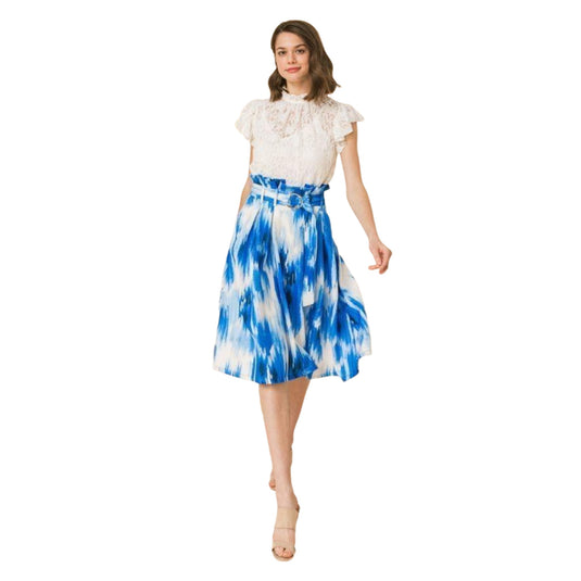 Elegant woman in a chic lace top and tie-dye blue midi skirt ensemble, complemented with beige high-heeled sandals, posing with one hand lightly resting on a vintage piano.