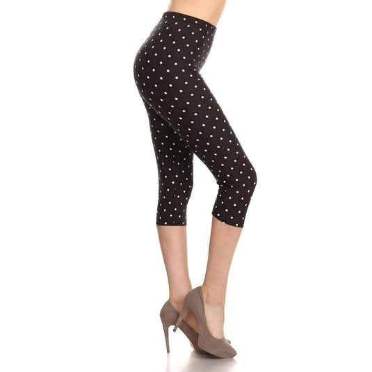 A woman models high-waisted capri leggings adorned with a classic white polka dot print on a black background, paired with elegant taupe high heels for a timeless and chic look.