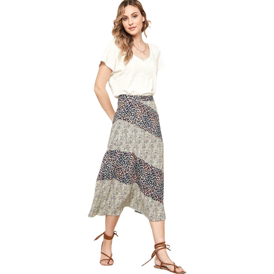 A woman in a casual white V-neck tee tucked into a flowing colorblock floral midi skirt, complete with beige and dark floral patterns, paired with brown sandals.