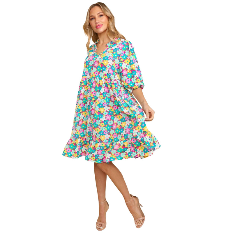 Load image into Gallery viewer, Front view of a woman wearing a vibrant bubble sleeve floral midi dress with ruffles in a mint and pink color scheme. She is standing gracefully with one hand holding the hem of her dress and a slight smile on her face.
