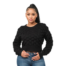A woman in a black puffy checker-pattern sweater and blue jeans stands confidently with her hand on her hip.