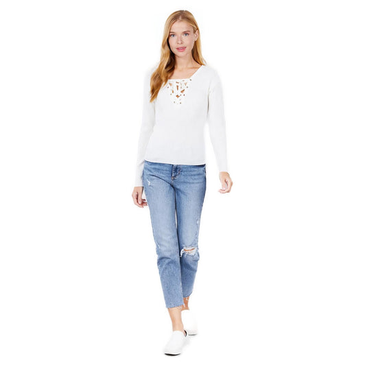 Confident woman in a chic white V-neck sweater with lace-up detail, paired with distressed blue jeans and white slip-on shoes, standing against a plain background.