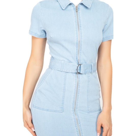 hree-quarter view of a woman modeling a light blue denim dress with a zipper front and belted waist. The dress is short-sleeved with a tailored fit, accentuating the model's silhouette.