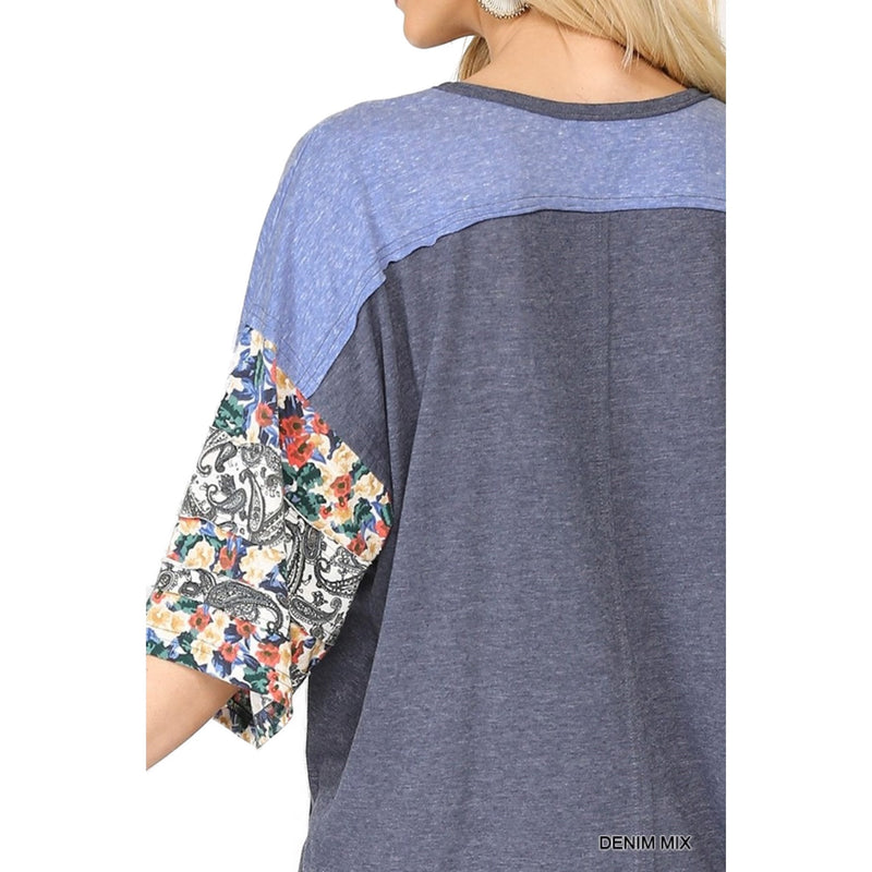 Load image into Gallery viewer, Close-up view of the back of a denim mix floral dolman top. The top has a blue and grey color block design with intricate floral patterns on the sleeves.
