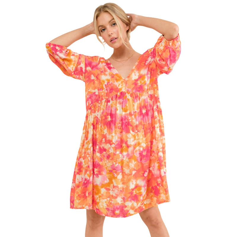 Load image into Gallery viewer, Woman wearing a vibrant floral dress with V-neck and puff sleeves, perfect for summer outings and casual events.
