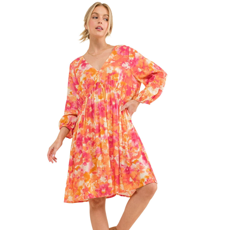 Load image into Gallery viewer, Front view of a woman in a bright floral dress with V-neck and puff sleeves, styled for a casual yet chic look.
