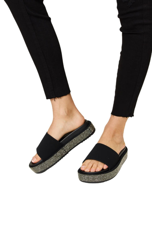 Side view of black rhinestone platform sandals – Featuring an open-toe design with sparkling rhinestones on the platform, paired with black pants.