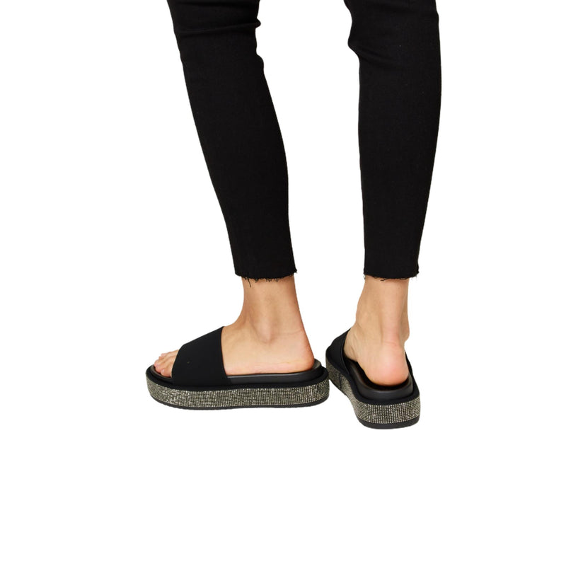 Load image into Gallery viewer, Back view of black rhinestone platform sandals – Highlighting the sleek back of the sandals paired with black pants.
