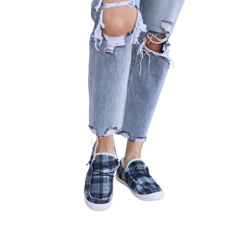 Load image into Gallery viewer, Another angle of the plaid plush sneakers paired with gray ripped jeans, showcasing the shoe pattern and denim frays.
