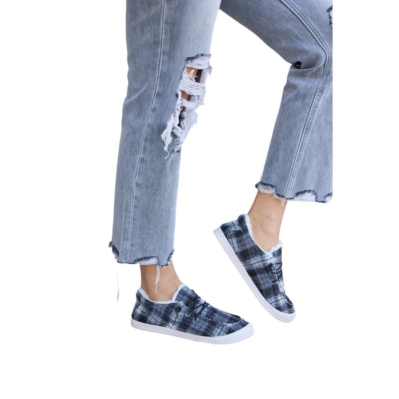 Load image into Gallery viewer, A close-up of a person wearing gray distressed jeans with frayed hems and plaid plush sneakers.
