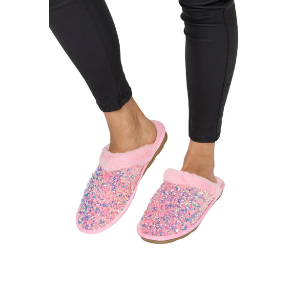 Close-up of pink sequin plush slippers with soft pink lining, worn by a person with black leggings. The slippers sparkle under the light, showing off the vibrant sequins.