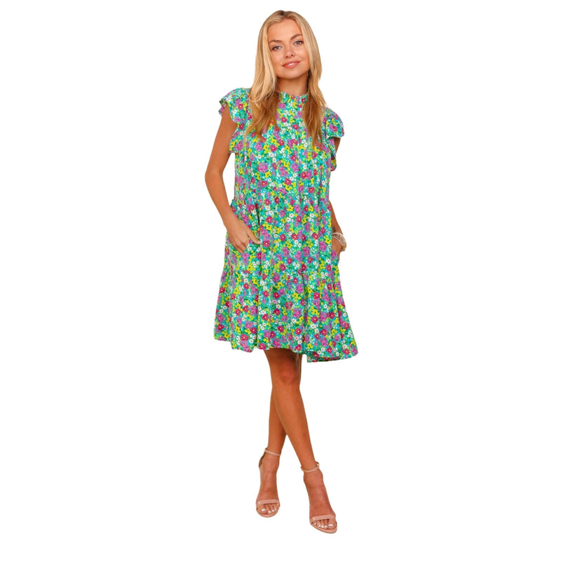 Load image into Gallery viewer, Front view of a woman wearing a bright floral print dress with a high neckline and short ruffled sleeves. The dress features a vibrant mix of green, pink, and blue flowers, with a relaxed, above-the-knee fit. The model is smiling and has her hands in the dress&#39;s pockets, showcasing its casual and fun style.
