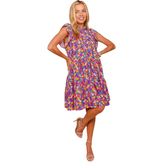  Woman posing in a frilled mock neck ditsy floral dress with bright floral patterns, standing with a smile.