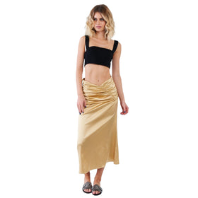 A woman wearing a golden satin ruched midi skirt paired with a cropped black tank top, standing confidently. The outfit combination suggests versatility, being suitable for both day and evening wear.