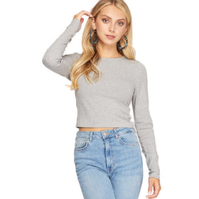 Confident woman in a grey long sleeve rib knit crop top, paired with light blue jeans, posing with hand on head.