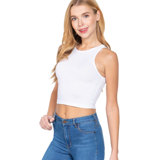 Displayed is a woman wearing a sleeveless white crop top and blue jeans. The top has wide shoulder coverage and a high neckline, offering a simple yet versatile look suitable for various occasions.