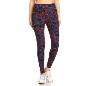 A model wears high-waisted leggings featuring a charming heart pattern in red and pink on a navy blue background, paired with classic white sneakers.