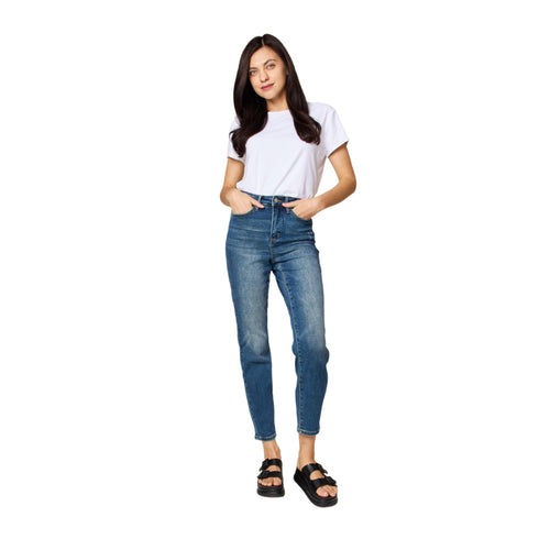 A model in a white t-shirt wearing mid-rise blue denim jeans with a slim fit, standing in a relaxed pose, hands in pockets, paired with black platform sandals.