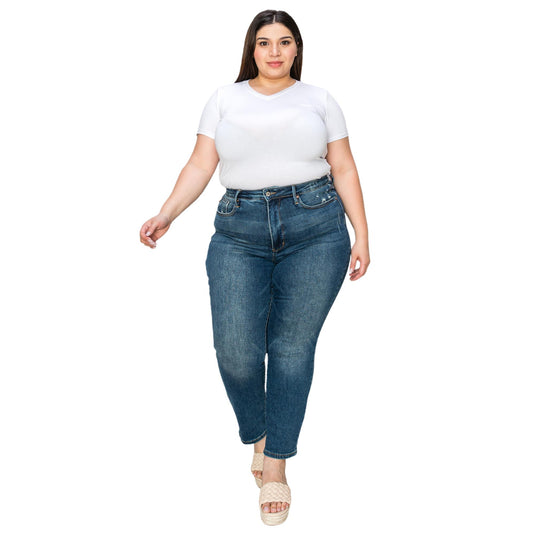 Plus-size woman confidently walking forward, wearing a white shirt tucked into high-waisted dark wash jeans with light distressing, paired with beige sandals.