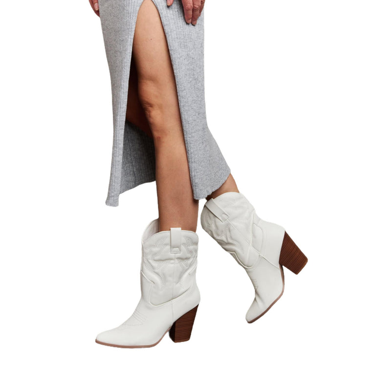 Load image into Gallery viewer, A side view of the model wearing white cowboy boots with a pointed toe and block heel, paired with a gray midi skirt that features a side slit. The stylish boots give a modern twist to classic Western fashion.
