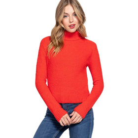 Model wearing a vibrant red fluffy turtleneck sweater and blue jeans, standing with a hand on her hip.