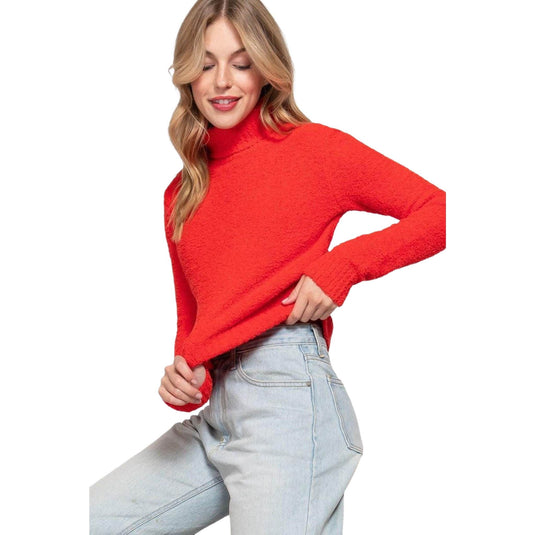 Fashion portrait of a woman in a bright red turtleneck sweater, casually tucking her hand into light grey jeans.