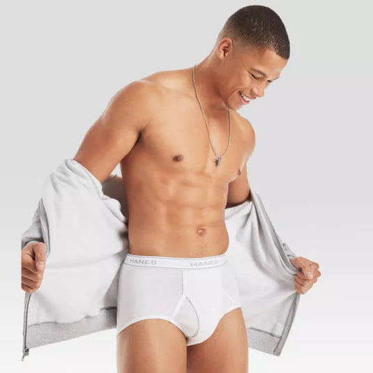 A smiling man with short hair, partially removing a gray jacket to reveal white Hanes tagless briefs, highlighting the fit and comfort.