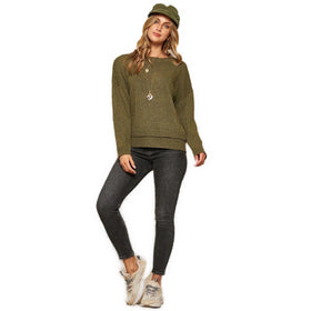 A fashion-forward woman in an olive hued knit sweater, fitted gray jeans, and stylish sneakers, completes her look with a matching olive beanie.