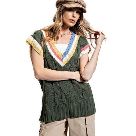 Front view of a woman wearing an oversized, olive green knitted sweater vest with multicolor stripe accents on the V-neckline and cap sleeves, paired with beige cargo pants and a matching cap.