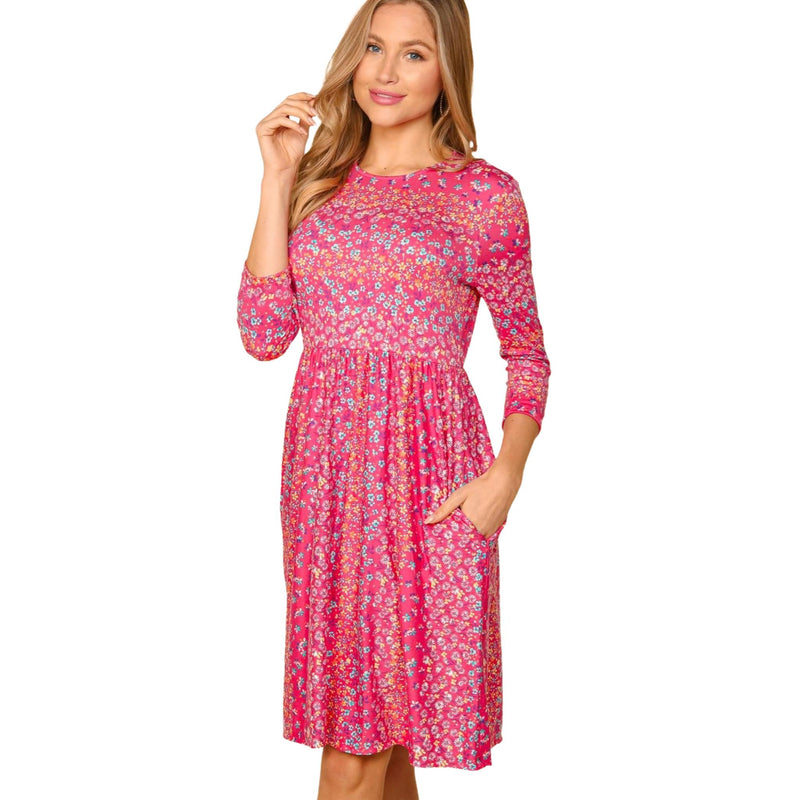 Load image into Gallery viewer, Woman in a pink floral dress with three-quarter sleeves, posing with one hand on her hip, showcasing the dress&#39;s vibrant pattern and pockets.
