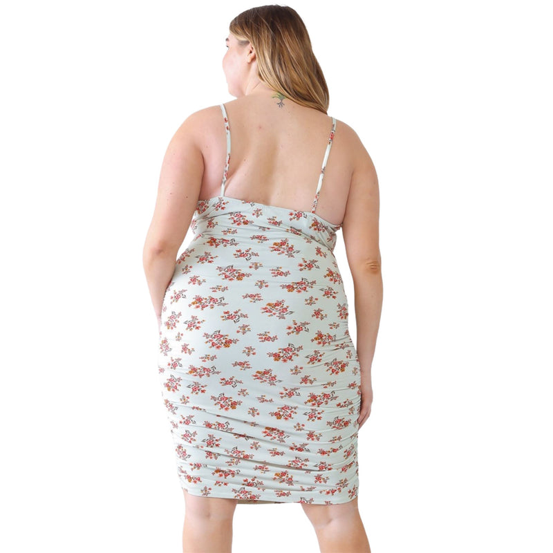 Load image into Gallery viewer, Back view of a plus-size model in a light floral ruched cami dress, highlighting adjustable straps and ruched detailing, paired with beige cowboy boots.
