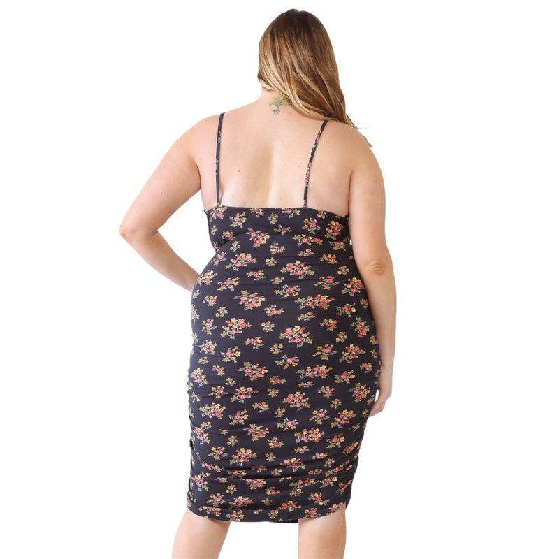 Load image into Gallery viewer, Back view of a plus-size model in a black floral ruched cami dress, showcasing adjustable straps and ruched detailing, paired with strappy black heels.
