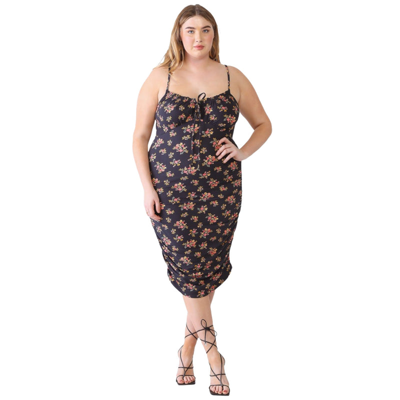 Load image into Gallery viewer, Plus-size model wearing a black floral ruched cami dress with front tie detail, standing with hands on hips.
