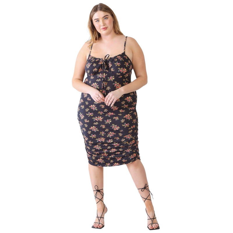 Load image into Gallery viewer, Plus-size model walking in a black floral ruched cami dress with a square neckline and front tie detail, styled with strappy black heels.
