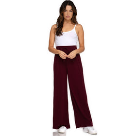 Front view of a woman wearing Wine-Colored Rib Knit Wide Leg Long Pants with a drawstring waist, paired with a white tank top, showcasing a comfortable yet stylish fit. The pants are available in sizes S, M, L.