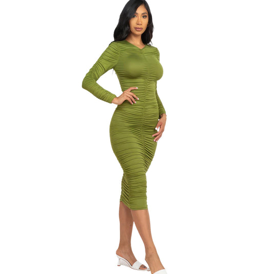 Chic woman models an olive branch green ruched long sleeve midi dress, paired with white open-toe heels for a refined look.
