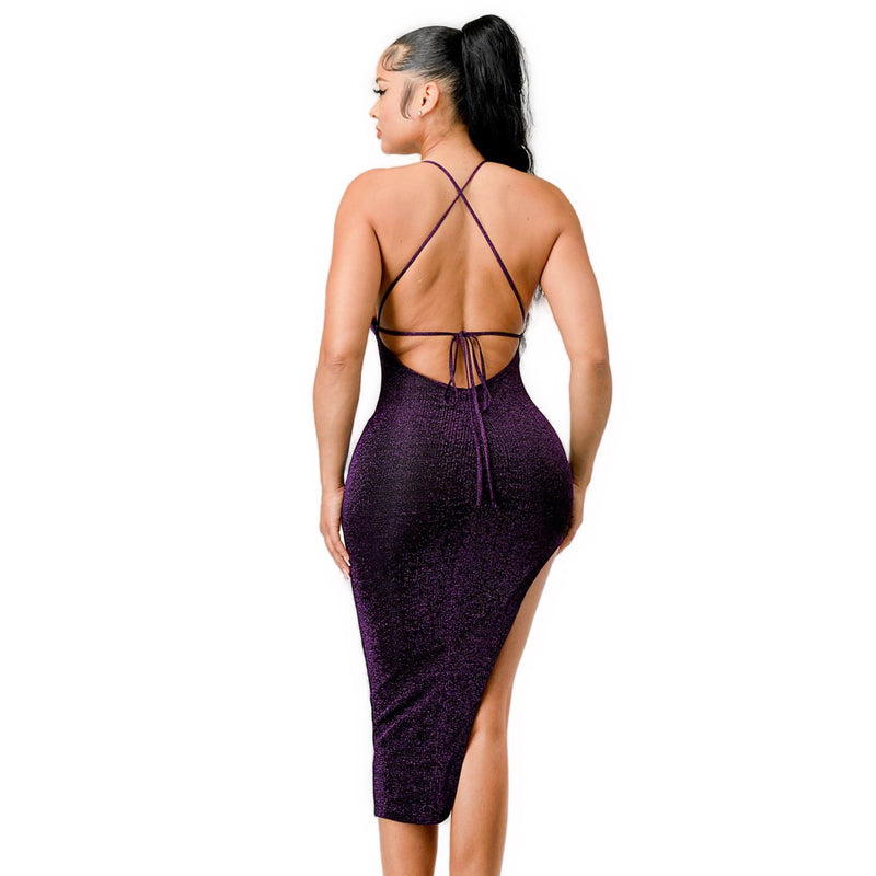 Load image into Gallery viewer, A woman wearing a purple, shimmering sweetheart midi dress. The dress features a backless design with crisscross straps and a high slit on one side. The model has her back turned, highlighting the intricate strap details and the curve-hugging fit of the dress.
