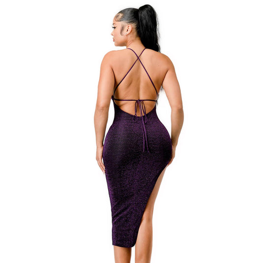 A woman wearing a purple, shimmering sweetheart midi dress. The dress features a backless design with crisscross straps and a high slit on one side. The model has her back turned, highlighting the intricate strap details and the curve-hugging fit of the dress.