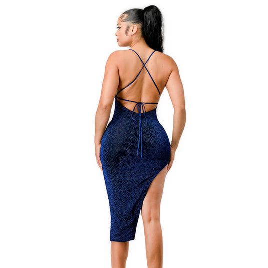  A woman wearing a royal blue, shimmering sweetheart midi dress. The dress features a backless design with crisscross straps and a high slit on one side. The model has her back turned, showcasing the intricate strap details and the curve-hugging fit of the dress.