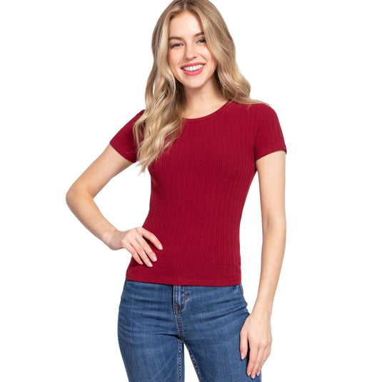 A woman models a rich crimson short-sleeve rib knit top, styled with sleek blue jeans. This top showcases a snug fit and a ribbed design, perfect for a bold yet sophisticated day-to-day look.