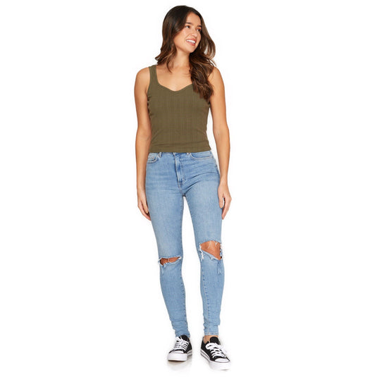 Full-body image of a woman wearing an olive green ribbed crop top with a scoop neckline, complemented by ripped blue jeans and casual sneakers.