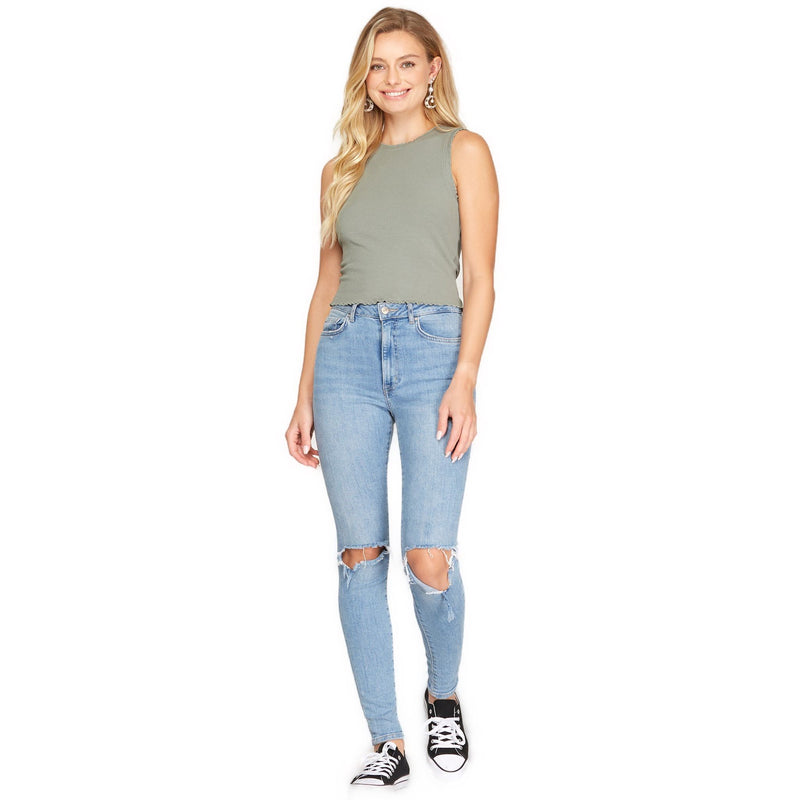 Load image into Gallery viewer, Full body image of a woman wearing a gray sleeveless rib knit top, featuring a ruffled trim and a comfortable fit, paired with ripped light blue jeans and casual sneakers.
