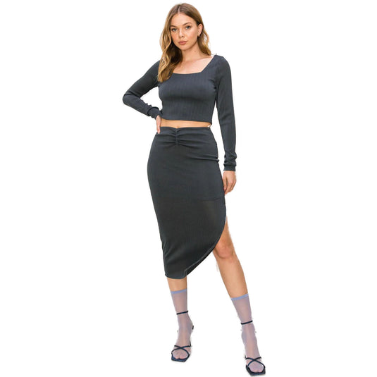 Full-length view of a woman posing in a coordinated charcoal ribbed outfit with a cropped top and high-waist midi skirt, complemented by elegant black heeled sandals.