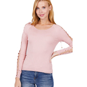 Close-up image of a woman modeling a soft pink ribbed sweater with unique strappy detailing on the sleeves against a white backdrop.