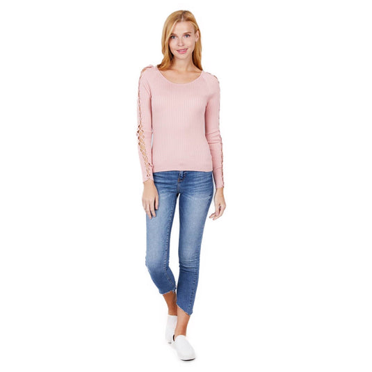Full body shot of a woman sporting a chic pink ribbed sweater with strappy sleeve design, complemented by fitted blue jeans and casual white footwear.