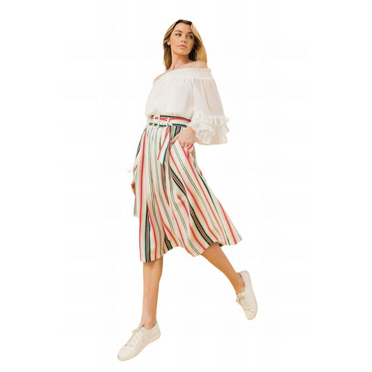 Full-body image of a model posing in a striped pleated midi skirt featuring a belted waist, paired with a white off-the-shoulder ruffle blouse and white sneakers, set against a plain background.